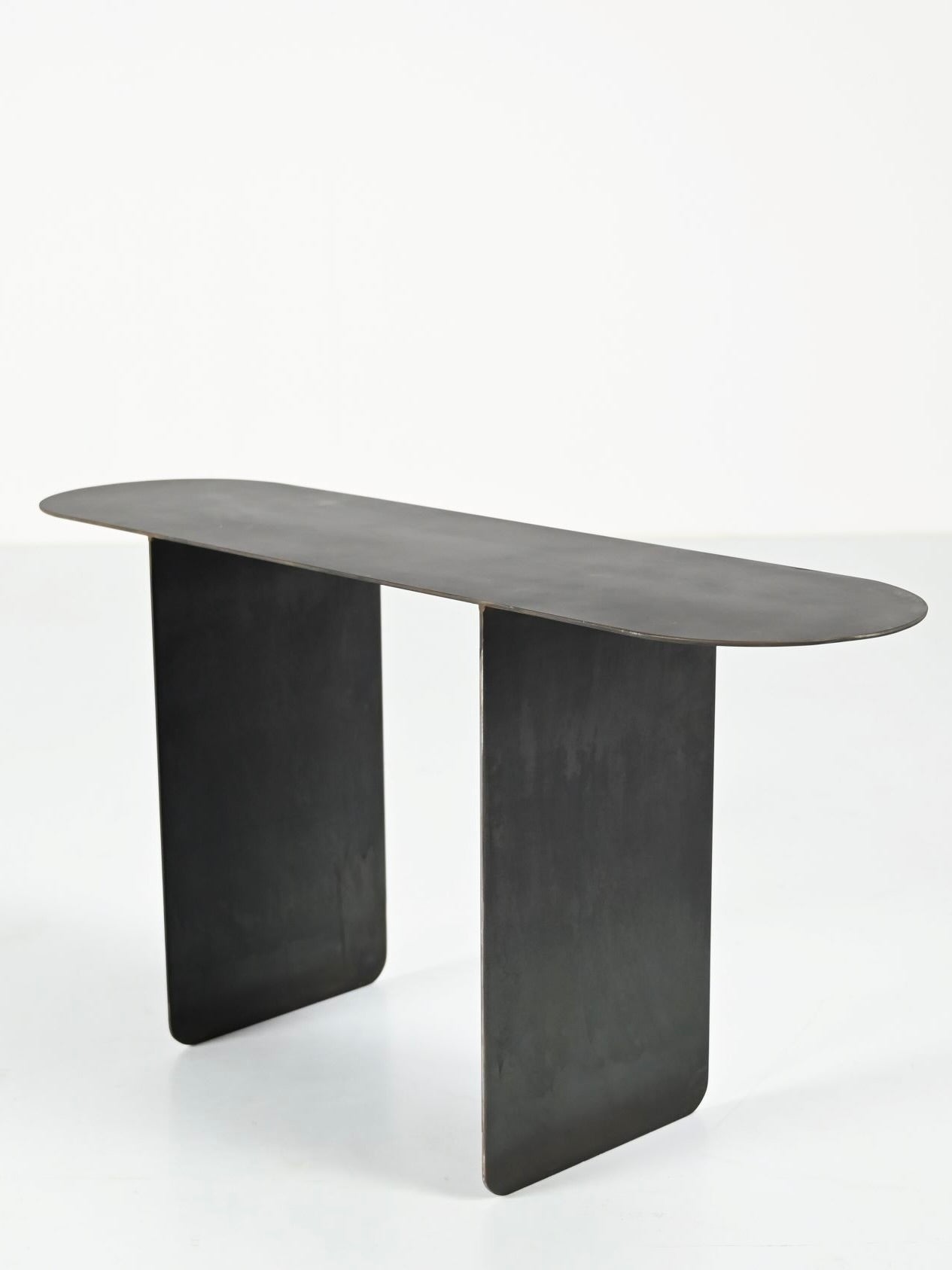 The Altar by COSEINCORSO is a sleek and modern black console table featuring an oval top supported by two rectangular legs. This limited edition piece showcases a minimalist design that stands out elegantly against a white background, evoking the simplicity of small altars.