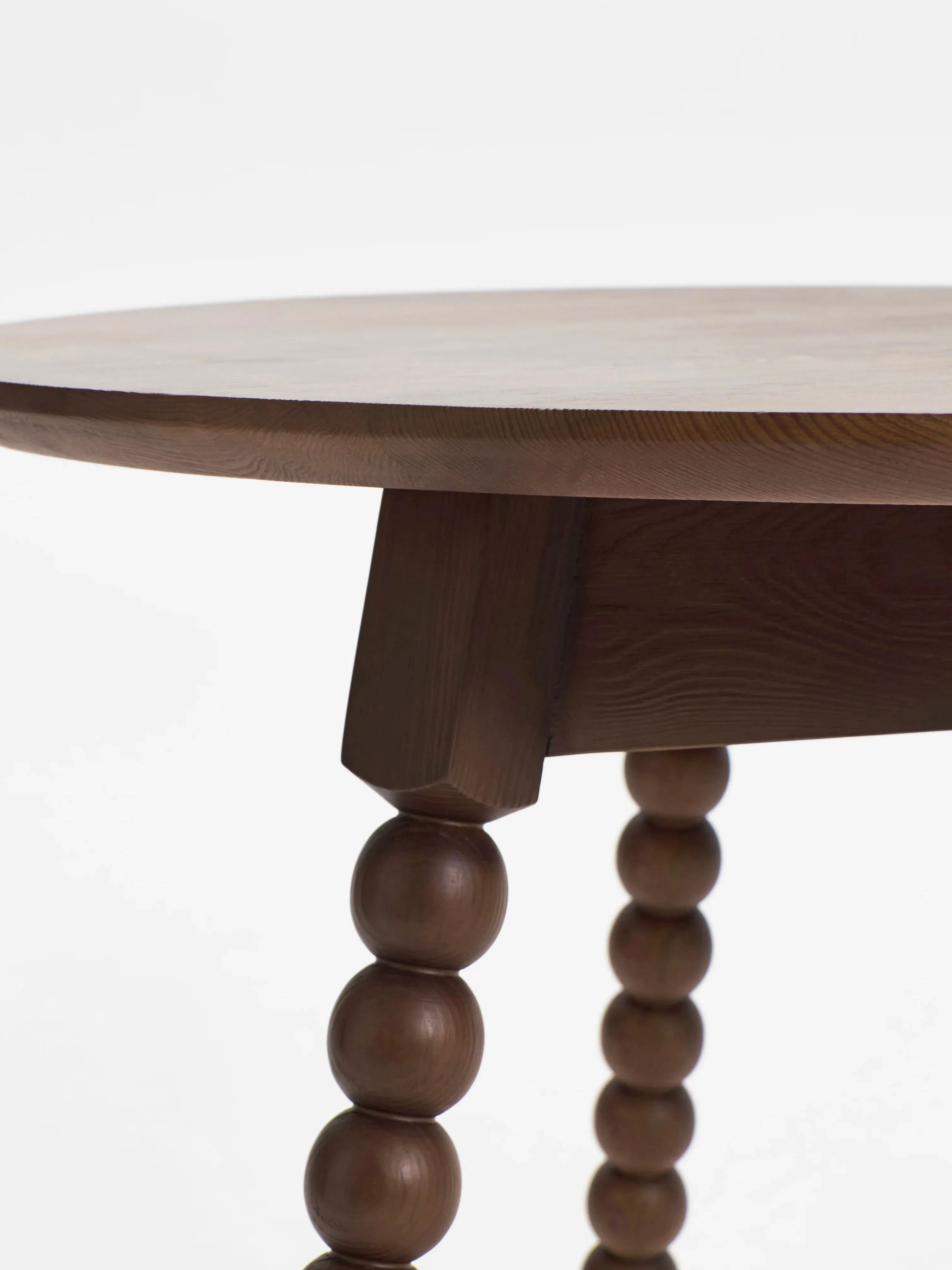 Close-up of the 'Bolha' Table by Project 213A, featuring a round top and intricately turned wood spheres for legs. Made from solid wood with a smooth finish showcasing visible grain patterns. The background is plain white.