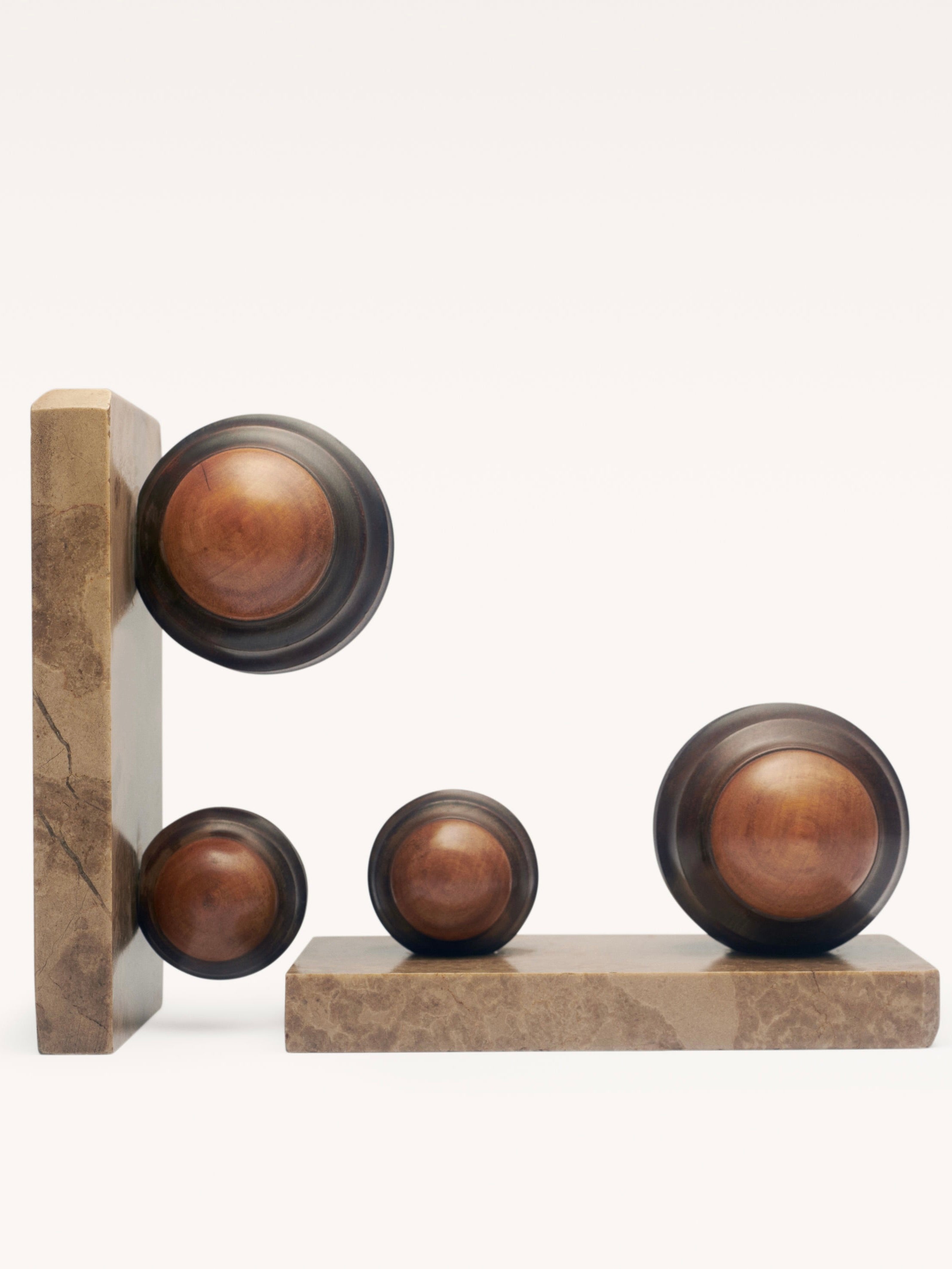 A Pair of Art Deco Paper Press by Galerie MLS features modernist spheres in diverse sizes creatively arranged on two brown stone slabs, achieving a balanced geometric composition against a plain backdrop that recalls Art Deco elegance.