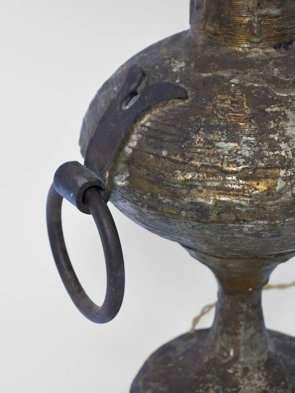 Close-up of a weathered, metallic object resembling the Max Bre Gilded Iron Brutalist Table Lamp from the 1960s, offered by Barracuda Interiors. It features a round base and protruding loop design. The surface displays signs of rust and tarnish, giving it an antiquated appearance against a plain, light-colored background that highlights its unique charm.