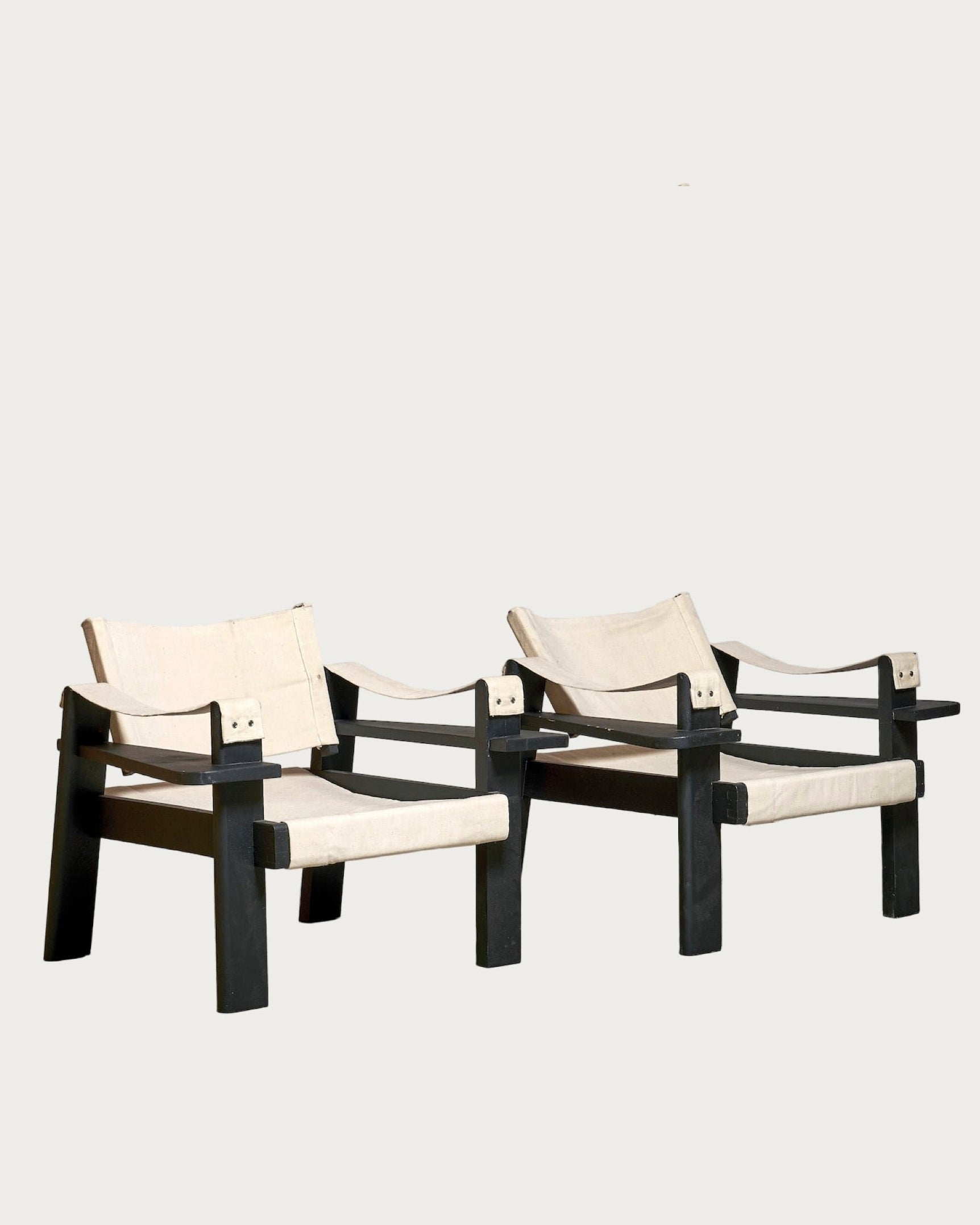 A Pair of Low Chairs in the Taste of Pierre Dariel by Harold Mollet, featuring black painted wood frames and off-white fabric seats and backs, are placed side by side on a plain light background.