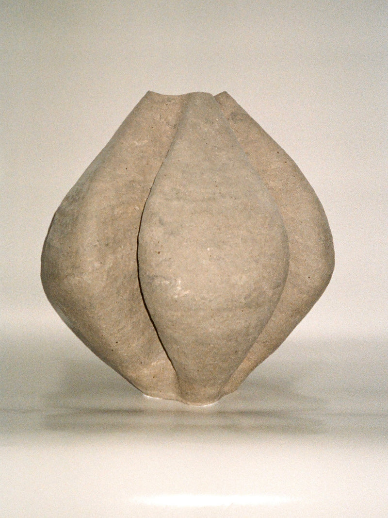 Growing Vase n.4 by Aiste Bagdonaite is a smooth, light-gray abstract sculpture with four curved, petal-like segments converging at the center, reminiscent of a handbuilt vase and set against a plain white background.