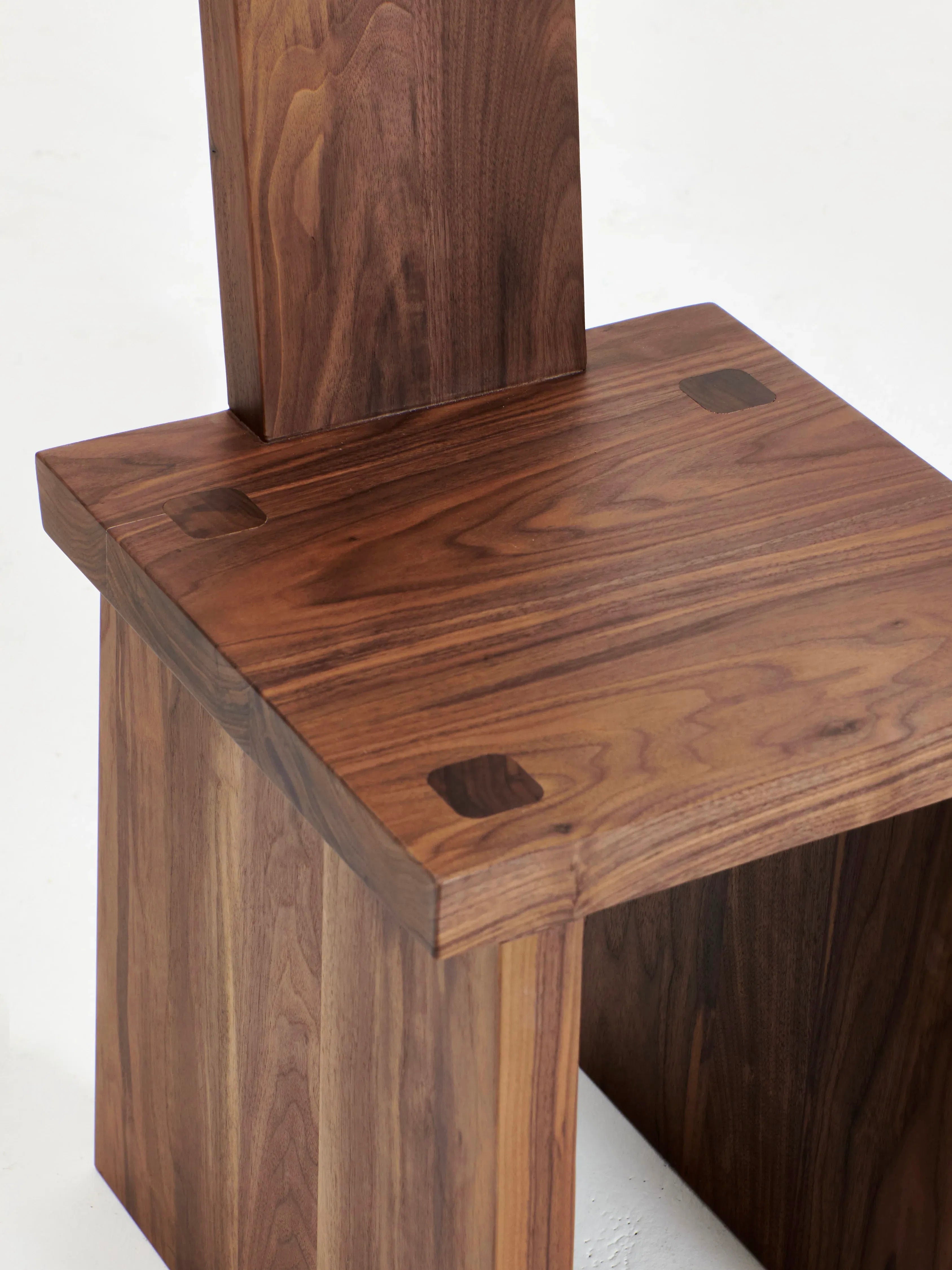 A close-up image of a Project 213A Portugal Chair No 4 showcasing its graphic backrest and seat. The chair is made of handcrafted walnut, featuring rich, dark wood with visible grain patterns. Four square wooden plugs are embedded at the corners of the seat, highlighting the chair’s artisanal craftsmanship.