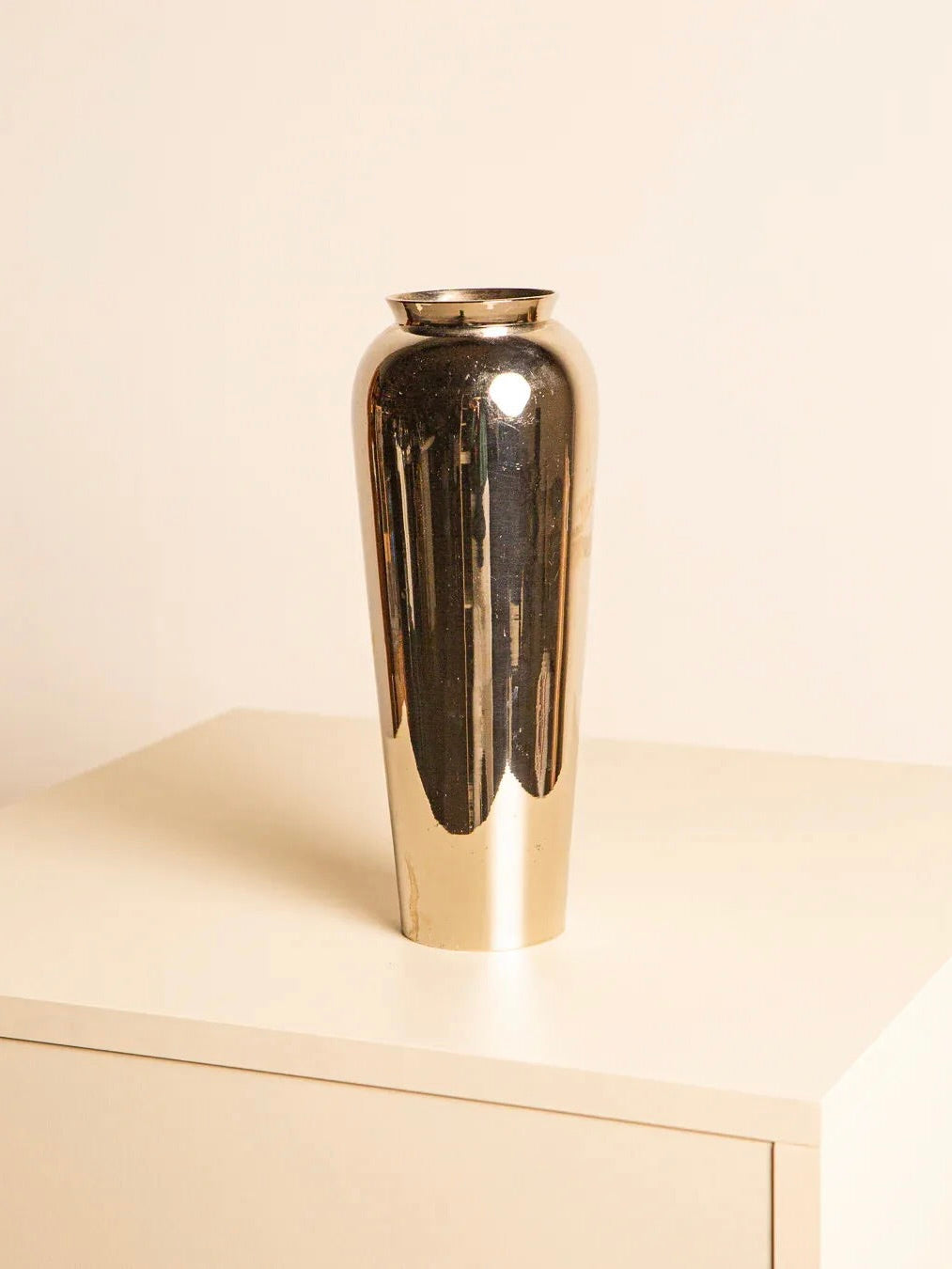 The Italian Silver-plated Vase 80's by Treaptyque features a tall, silver-plated design with a shiny, reflective surface that captures the essence of 1980s style. Crafted in Italy, it graces a light-colored table against a neutral background with elegance.