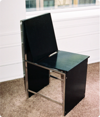 Minimalist black and metal chair placed on a carpeted floor in a bright room.