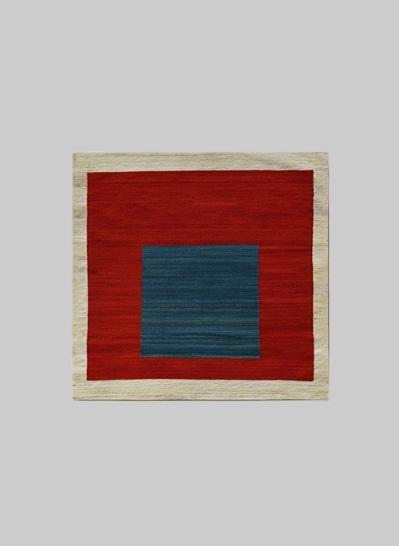 The ISHKAR Squares Kilim Pomegranate - Handwoven Rug featuring a bold design. Handwoven from wool and colored with natural dyes, it boasts a wide beige border, a large red field in the middle, and a smaller, centered blue rectangle. The contrasting colors create a striking geometric pattern.