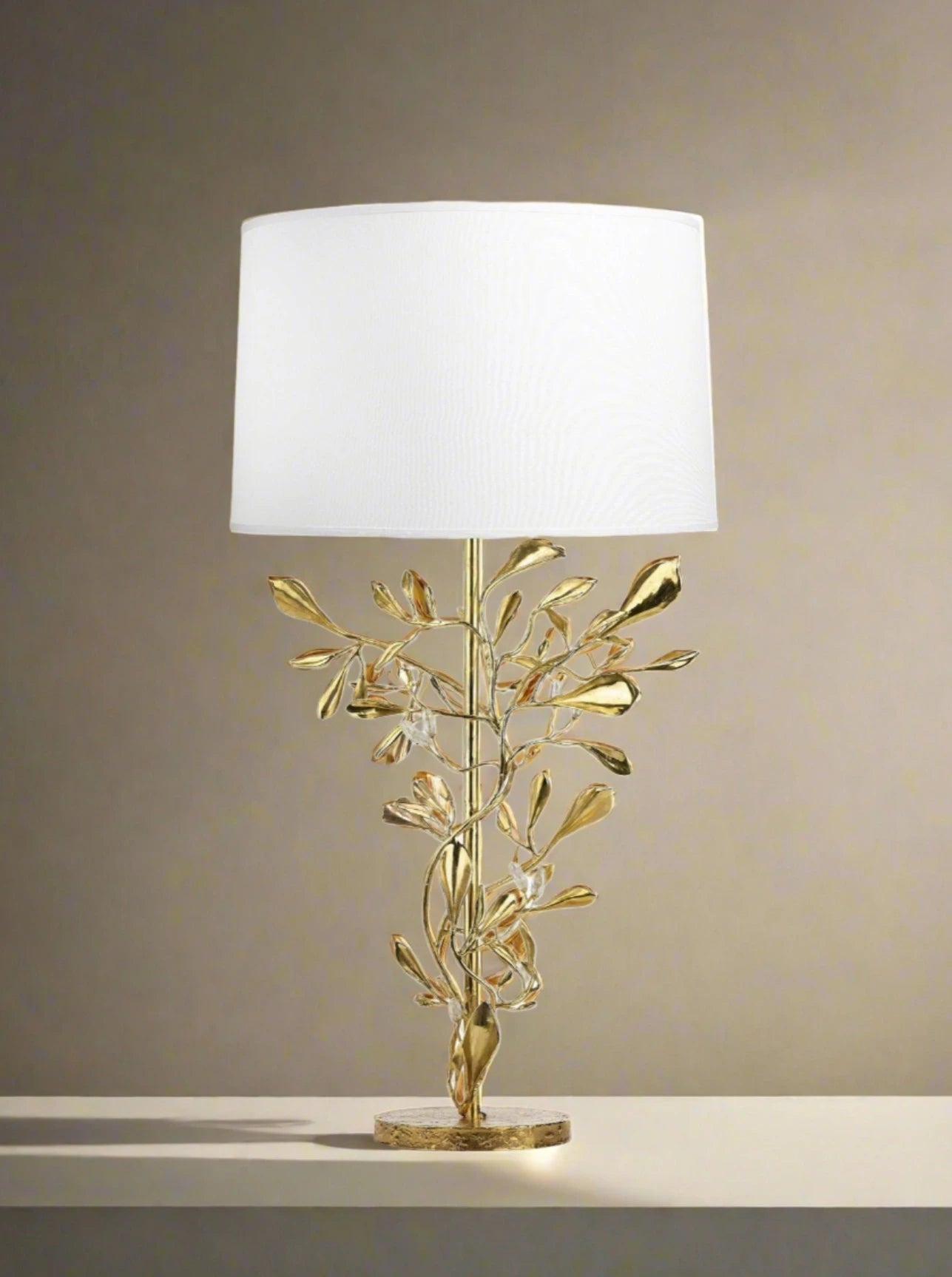 A decorative Foliage Table Lamp featuring a golden branch with leaves as the base and a simple white lampshade from the House of Goossens Paris.