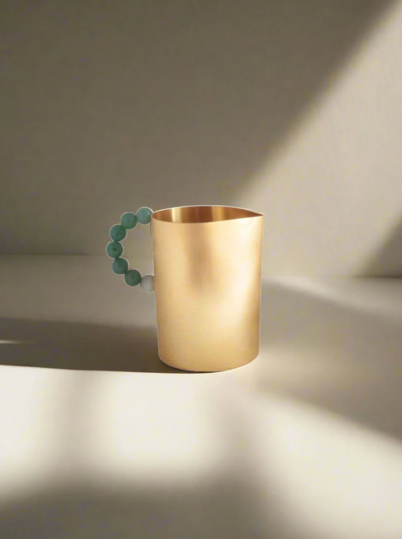 A Milk Perlina mug with a unique handle adorned with spherical green quartz beads, displayed against a plain white background by Natalia Criado.