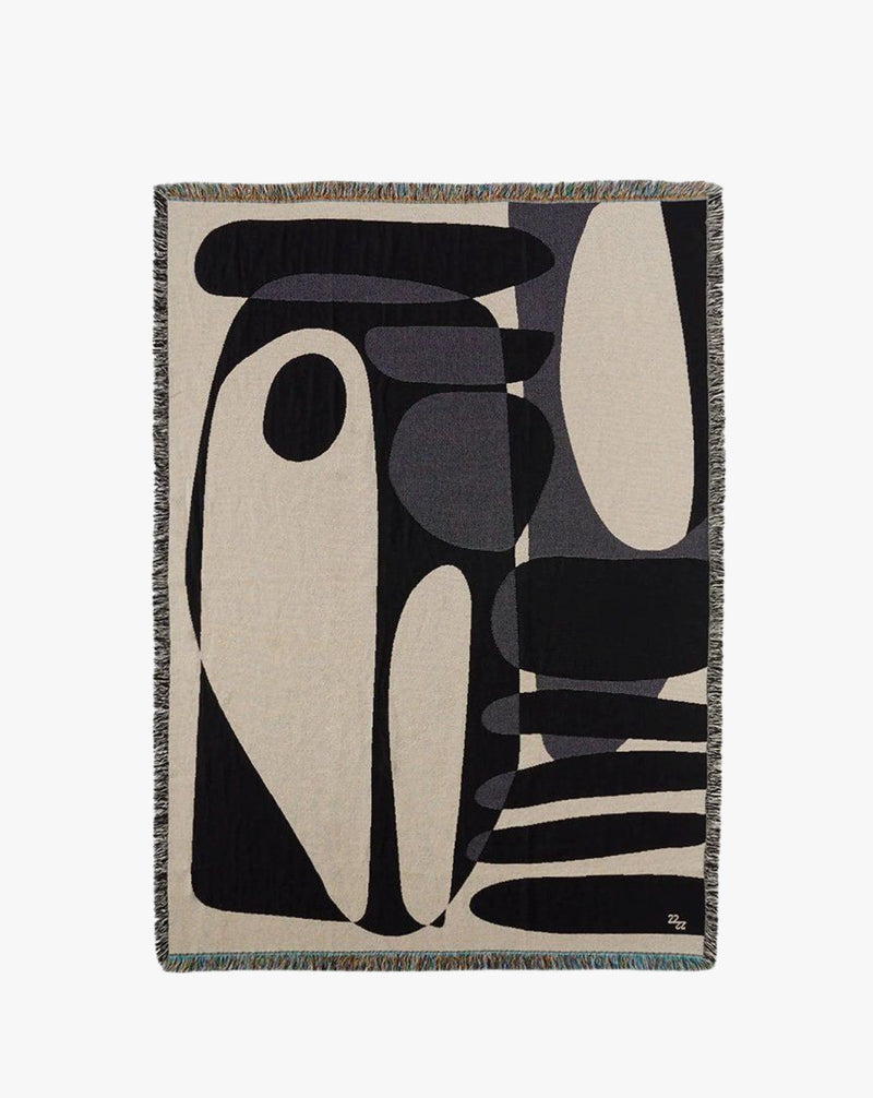 The Rokko Jacquard Throw by 2222Studio features a minimalist design with black, gray, and white organic shapes on a neutral backdrop. Its fringed edges and overlapping rounded forms add a luxurious touch to any interior space.
