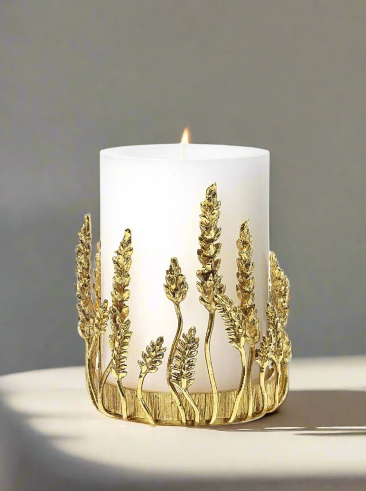 A Goossens Paris decorative candle with a gold wheat sheaf motif encircling its base, set against a plain white background, placed in a brass Wheat Candle Holder.