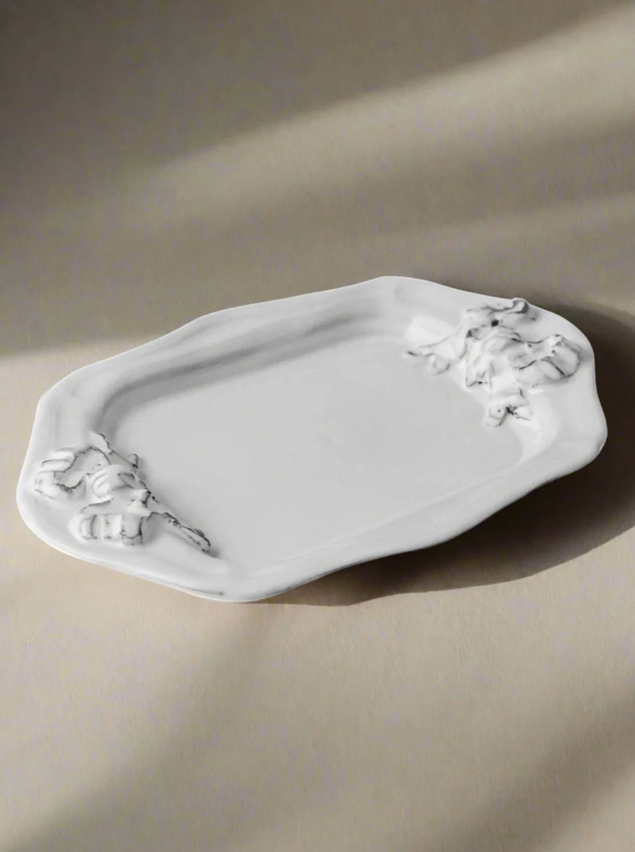 An elegant white enameled terracotta clay tray with ornate floral details at the corners, isolated on a white background, the Marie-Antoinette Ribbon Rectangular Platter by Carron.