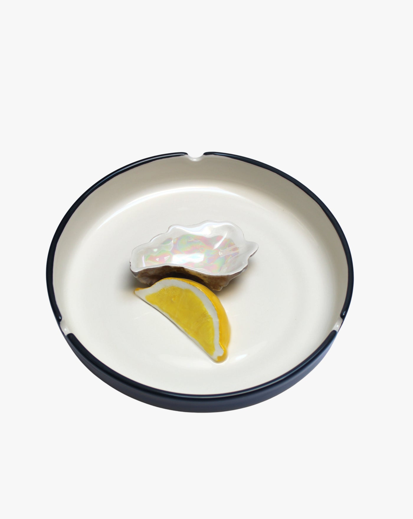 A single fresh oyster accompanied by a lemon wedge is served in a Villa Arev Plaisir Solitaire Ashtray against a white background.