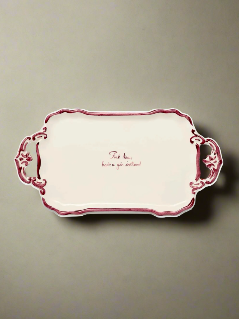 A decorative "F*ck Tea" Tray by Musae Studio, featuring ornate handles, red edging, and an inscription in the center that reads "Take less, you're a gem instead." Perfect for drink service or gin lovers, this rectangular ceramic tray is placed against a plain, neutral background.