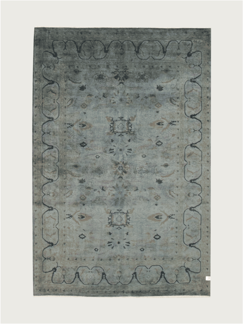 The Overdyed Rug in Indigo by catalog:three is a rectangular, hand-knotted piece measuring 183 x 274 cm. It boasts a vintage-style with a faded blue-gray hue, intricate floral patterns, scalloped border designs, and subtle motifs for an elegant and classic look.