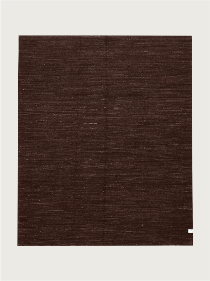 A unique large square Flatweave Rug in Walnut (244 x 292 cm) by catalog:three, set against a light background. It features a subtle weave pattern with a small white label in the bottom right corner, showcasing its wool hand-woven kilim craftsmanship.