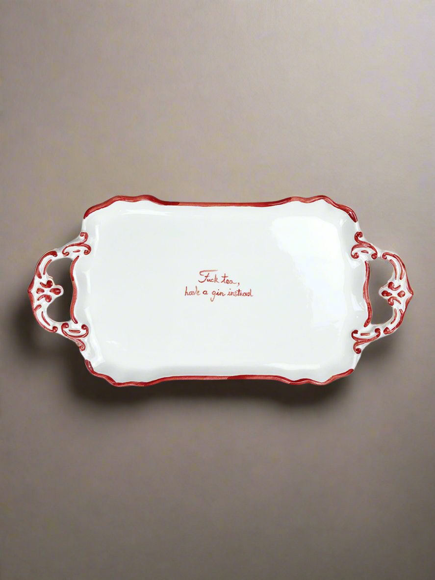 Musae Studio's "F*ck Tea" Tray is a decorative ceramic piece with ornate handles and red trim. Ideal for gin lovers, it features the phrase "Sack tea, have a gin instead" against a plain gray background.