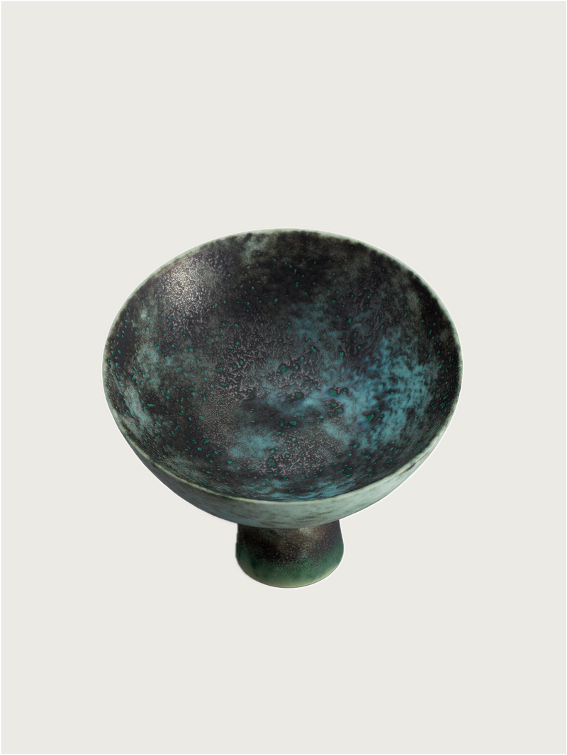 The Terra Bowl on Stand - Medium by Lobjet is a ceramic piece with a wide, shallow shape, footed design, and textured surface in dark green and blue, finished with an oxidized bronze glaze and set against a plain light background.