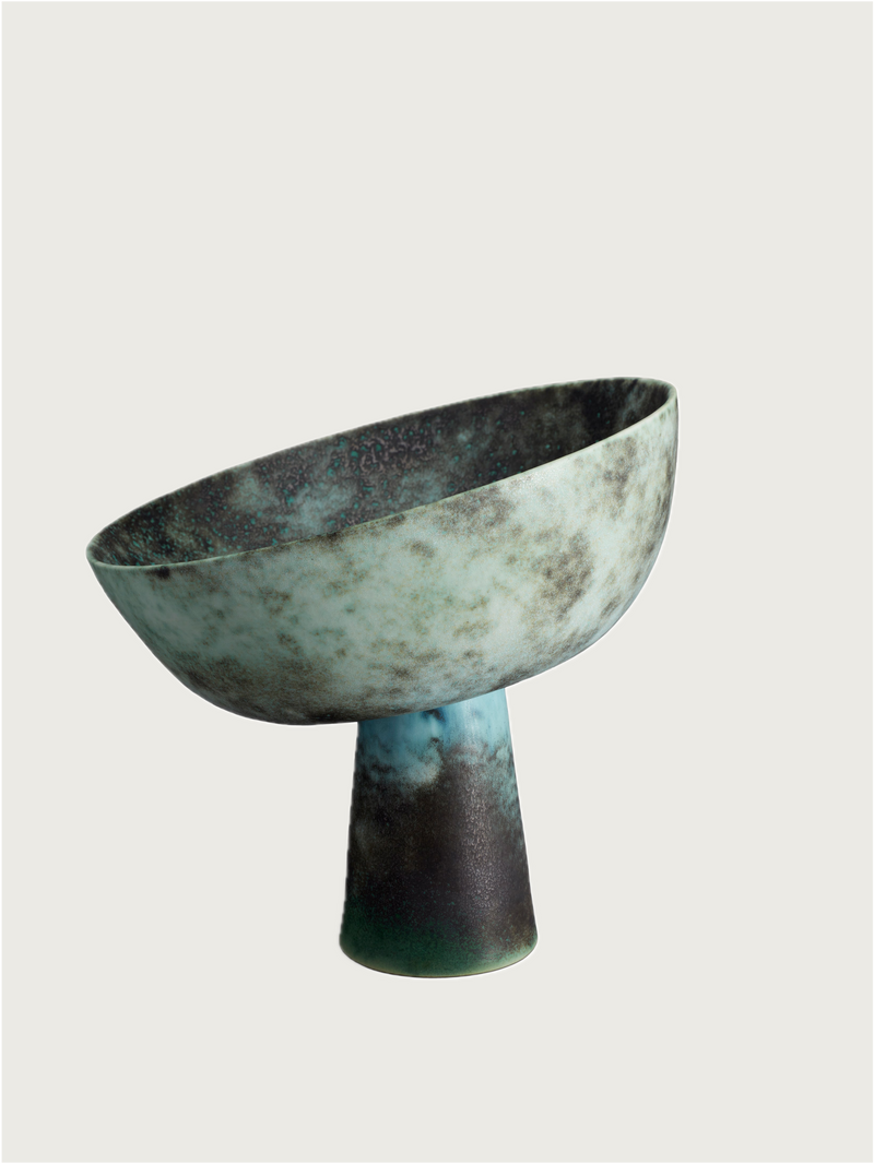 The Terra Bowl on Stand - Medium by Lobjet features a wide, tilted rim and narrow base with a textured, mottled surface in green, blue, and brown, reminiscent of oxidized bronze, shown against a plain light background.