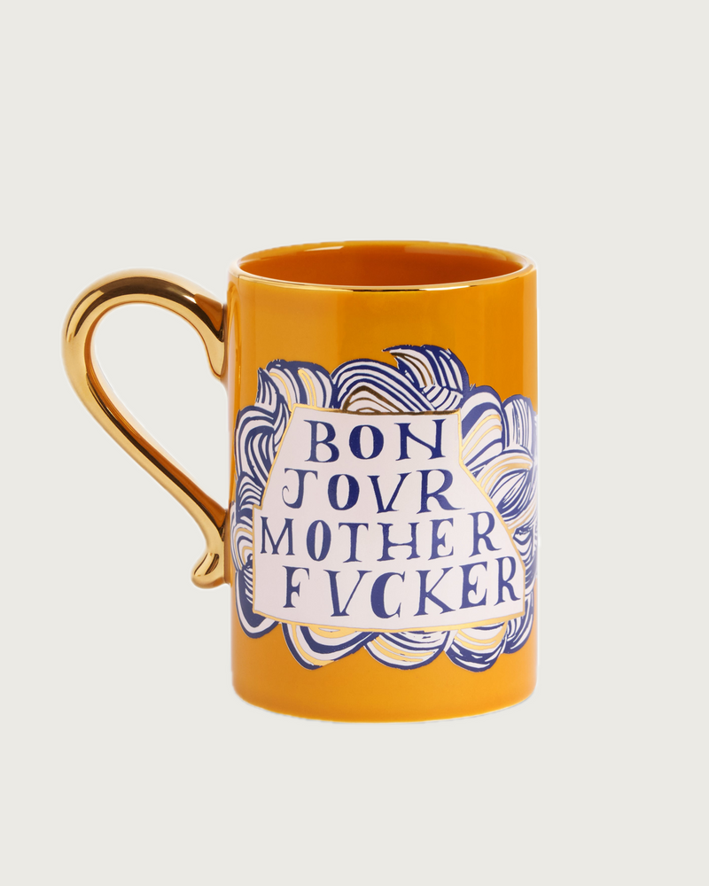 The Ruan Hoffmann Mother Fucker Mug by Lobjet is a bright orange mug with a shiny 24K gold handle and bold blue handwritten “BON JOUR MOTHER F\*CKER” text on a white cloud-like background with blue swirls.