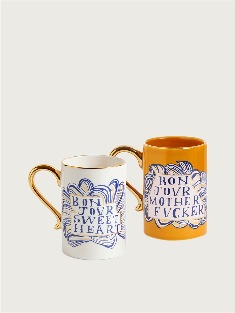 The Ruan Hoffmann Sweetheart + Mother Fucker Mugs Set of 2 by L'objet features white and orange ceramic mugs with gold accents, royal blue swirl designs, and bold phrases for a playful touch.