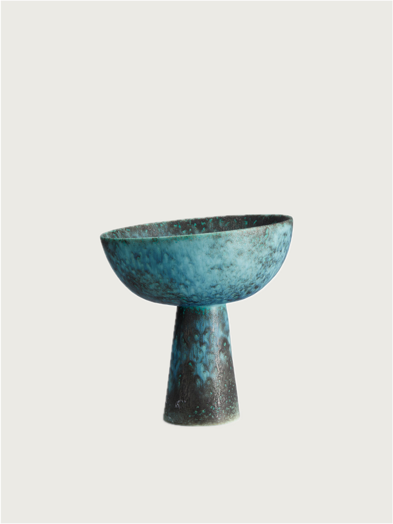The Terra Bowl on Stand - Small by L’Objet features a blue-green hue with a wide rim and conical base, inspired by the Cenote collection, and is displayed against a plain, light background.