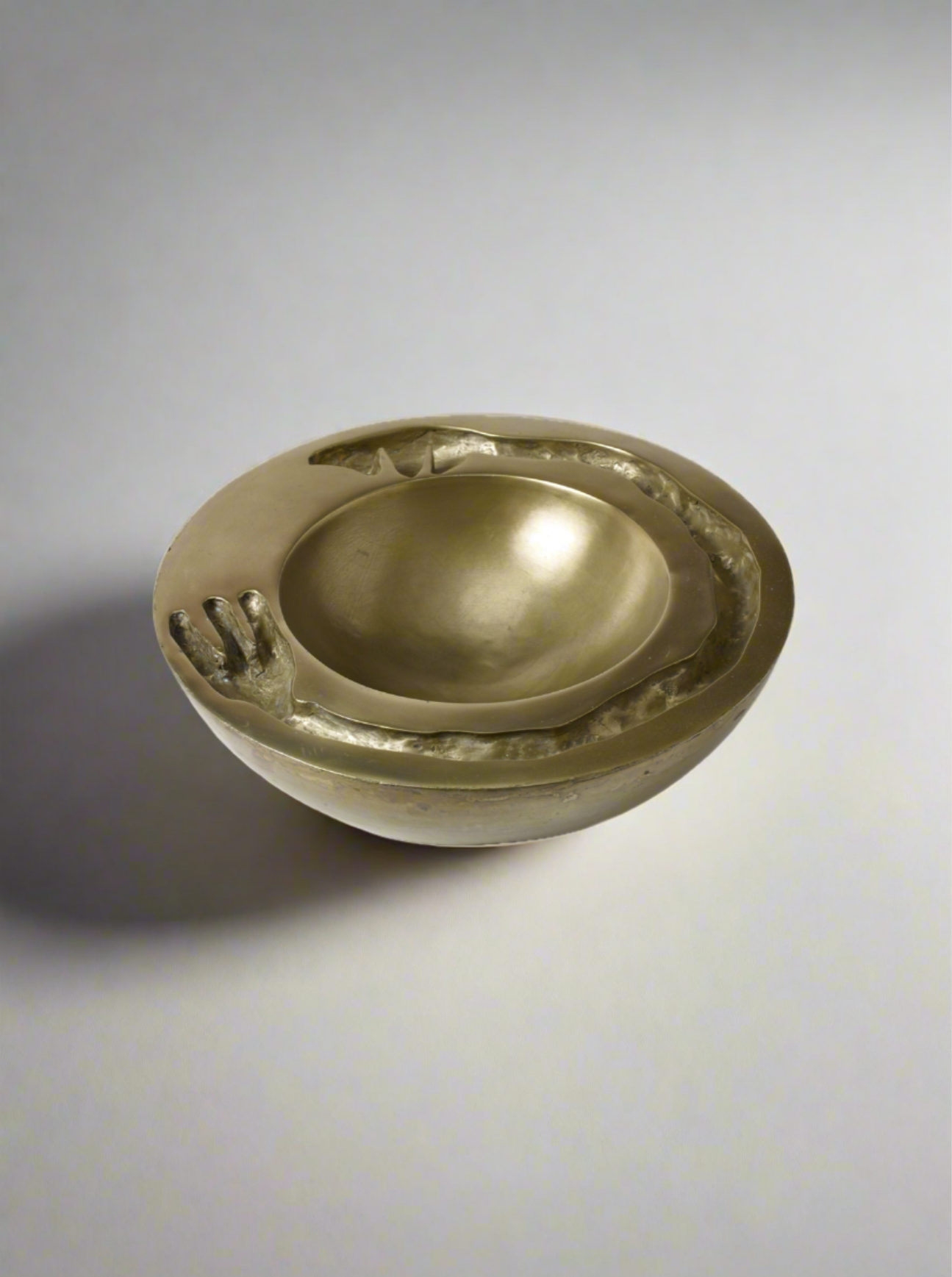 A Signature Dish Brass Sculpture by Lucy Page featuring an embedded hand design on the rim, placed against a plain white background.