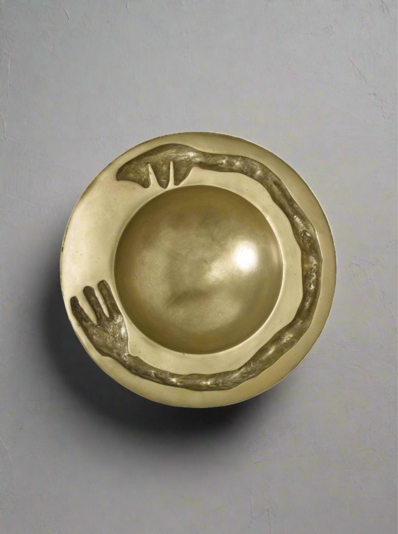 A handcrafted Lucy Page brass doorknob with an artistic motif featuring a hand slightly curved around one edge, giving a stylized and elegant appearance. The background is plain, highlighting the knob's shiny texture.