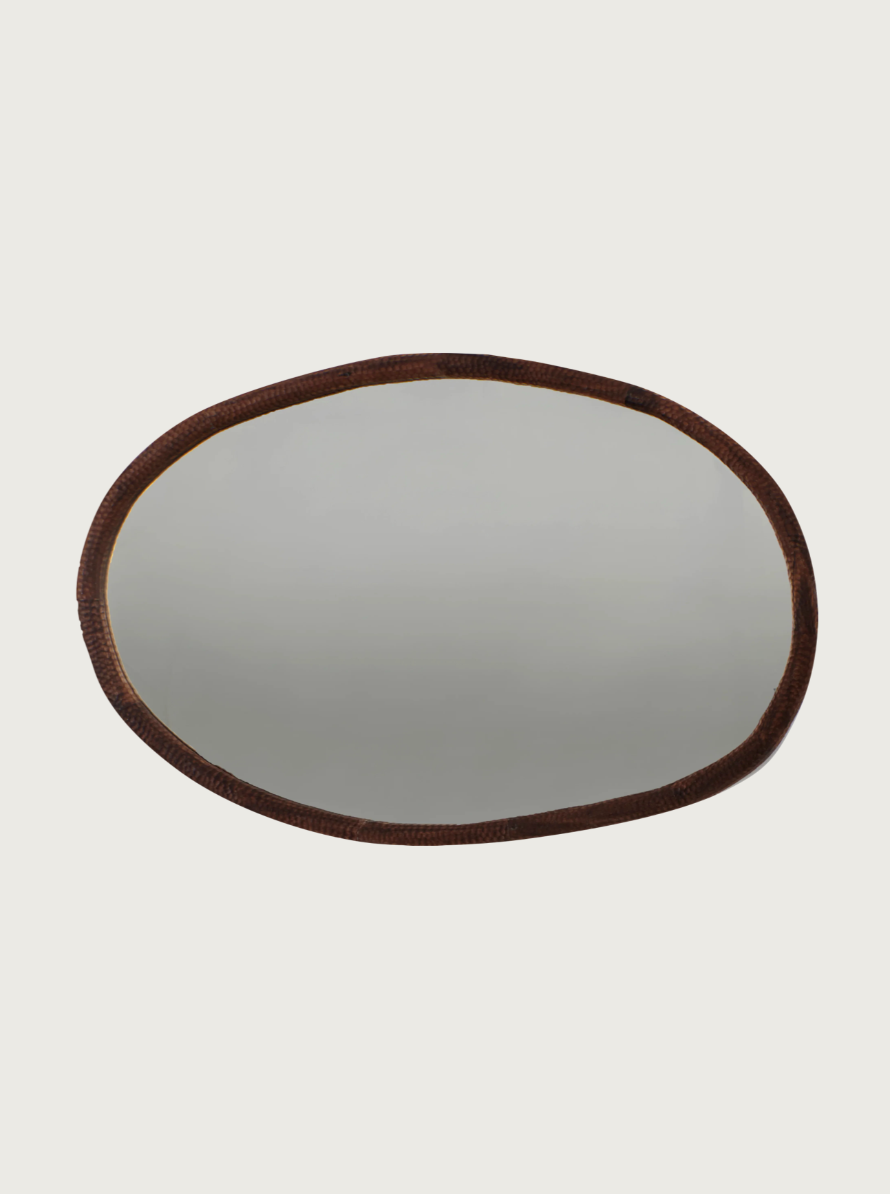 The Amarante Mirror oval from Project 213A features a simple, dark brown, textured frame carved from solid walnut. Set against a plain white background, its clear surface beautifully reflects a light, neutral-colored area.