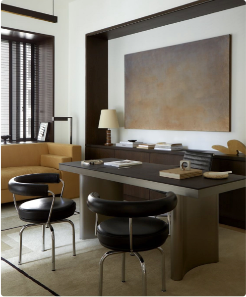 Home office with a sleek wooden desk, black leather chairs, abstract wall art, and a modern aesthetic featuring neutral tones.