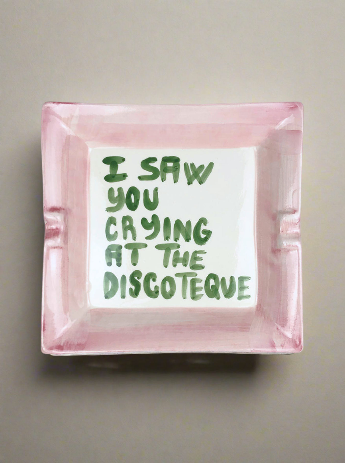 Musae Studio's "I saw you crying at the discoteque" ashtray features a square ceramic design with pink edges and a nostalgic green text message in the center, set against a neutral background.