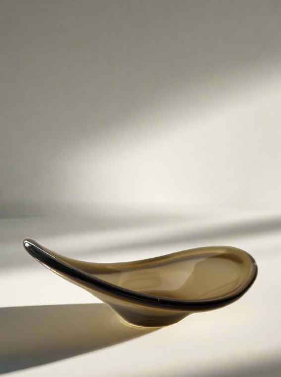 A Vintage Italian Murano Glass Dish by Flock Studio, featuring an elegant abstract design with smooth curves and an asymmetrical form, set against a soft, light-filled background that casts gentle shadows.