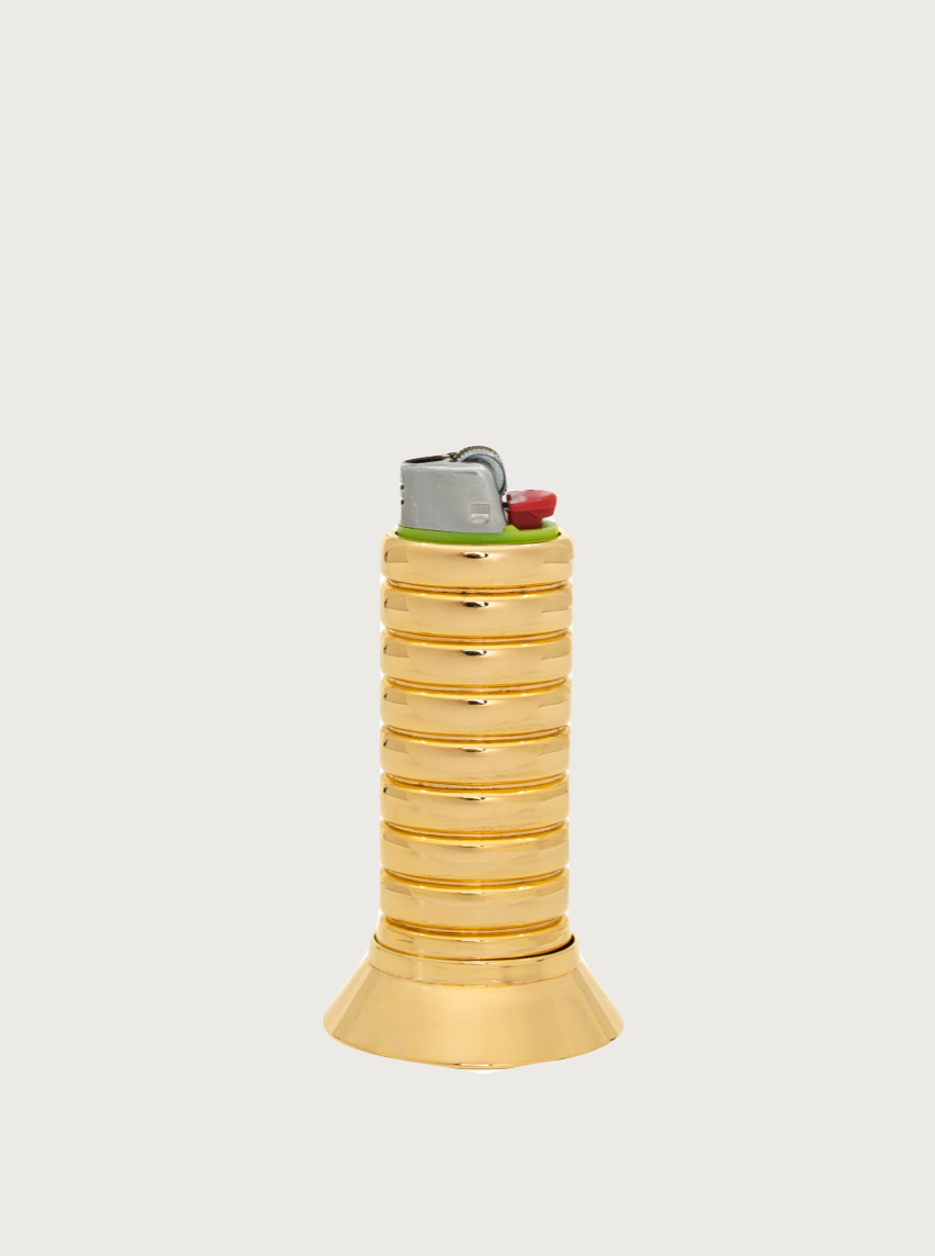 An ornate gold pocket lighter with a ribbed cylindrical body and a flared base stands against a plain white background. The FRY POWERS Gio Lighter Holder features a standard mechanism at the top, complete with a silver and red ignition button.