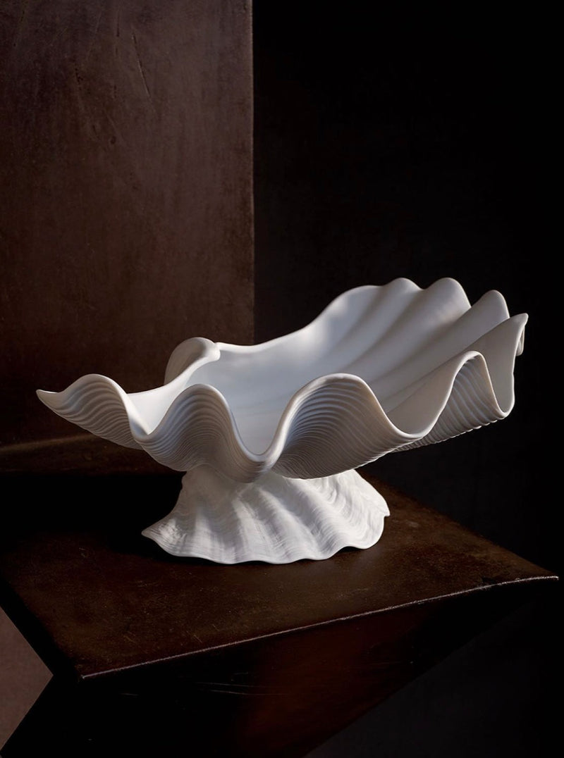 A sculptural white Neptune Bowl X-Large from the LOBJET Atelier Collection with undulating edges is displayed on a dark, rustic wooden table, against a dark backdrop, emphasizing its unique, Wabi-Sabi-inspired design.