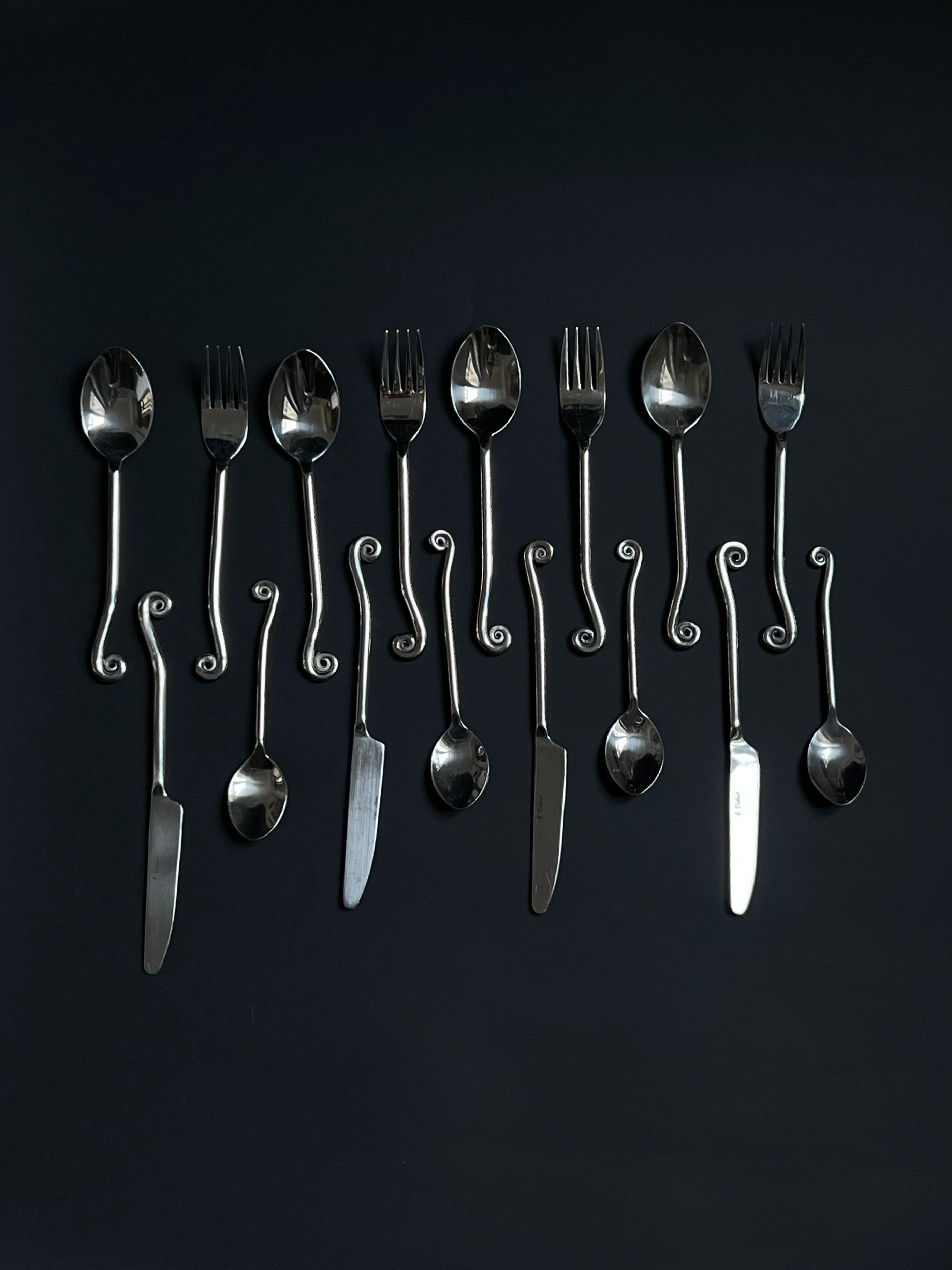 A set of Manushi Vintage Swirl Cutlery with ornate, twisted handles, including forks, knives, and spoons, arranged in a row on a dark background.