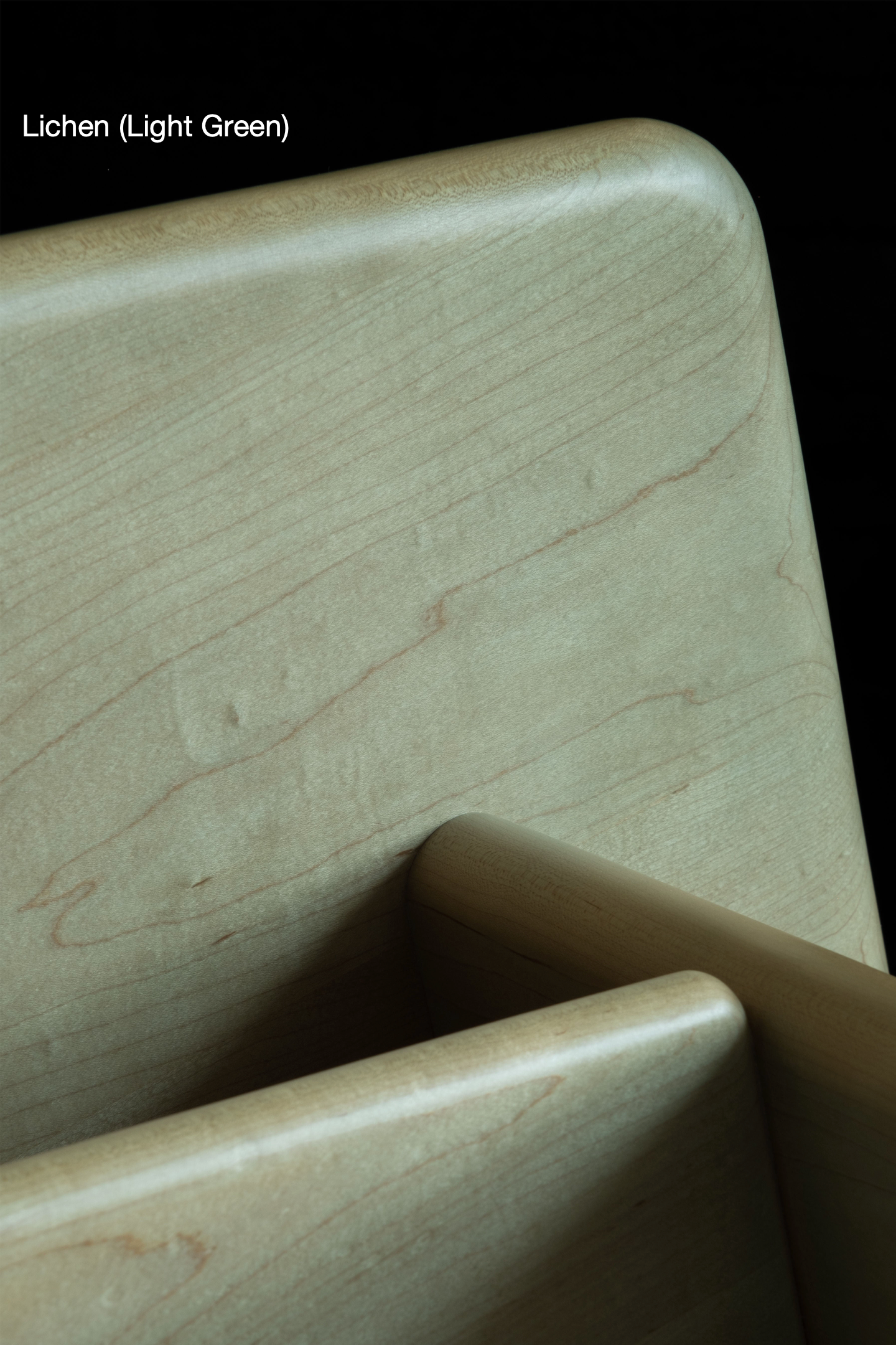 Close-up of the Arc Bench by Juntos Projects, featuring light-colored wooden furniture with rounded edges, stacked in front of a dark background. The grain of the wood and subtle details are visible, showcasing its premium natural materials. In the top left corner, the text "Lichen (Light Green)" is written.