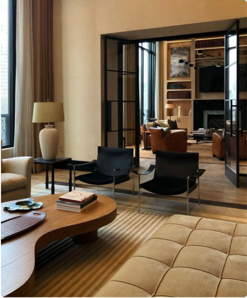 Modern living room with black armchairs, beige sofa, and a coffee table, featuring floor-to-ceiling glass doors leading to a cozy seating area with a fireplace