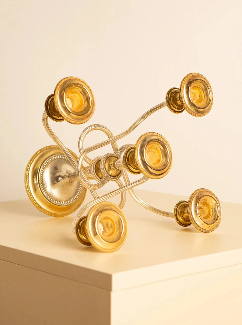 A Treaptyque Bougeoir italien "Medusa" en métal doré 70's with six candle holders arranged in a curvy, artistic design reminiscent of 60s aesthetics sits on a beige surface against a light background. The chandelier's metal frame has a polished, reflective finish, giving it an elegant look akin to a Medusa candlestick.