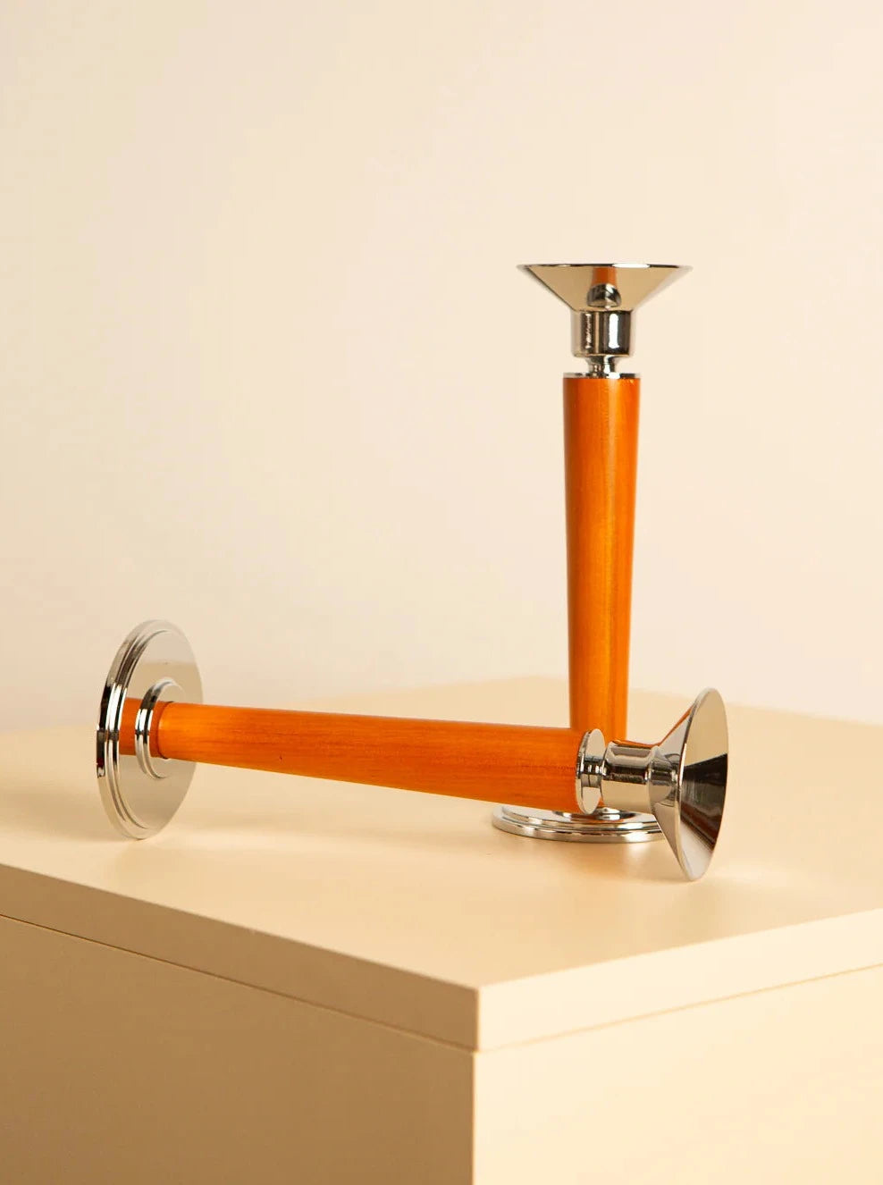 Two elegant Treaptyque Pair of 80's Italian wood and metal candleholders with polished silver bases and tops, and sleek orange wooden stems exhibit timeless charm. One candlestick stands upright while the other lies horizontally on a beige surface against a light background, evoking a touch of '80s design.