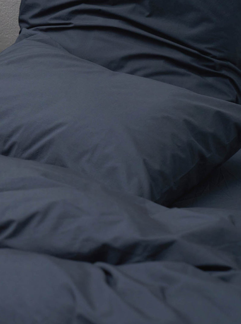 A close-up of a neatly made bed with MOST's Cotton Percale in Stormy comforter cover and pillows, focusing on the soft folds and creases of the fabric.