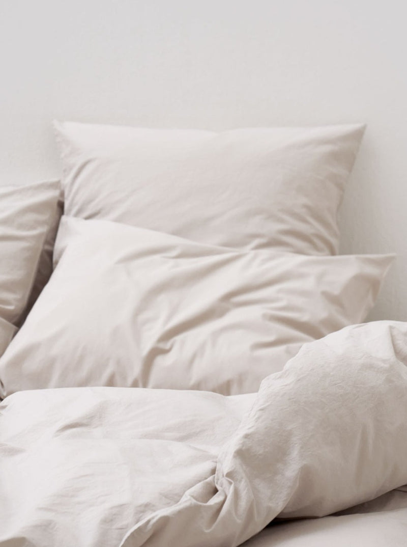 Two plush pillows on a bed, covered with MOST's Washed Cotton Percale Bed Set in Sand in a tranquil setting illuminated by soft natural light.