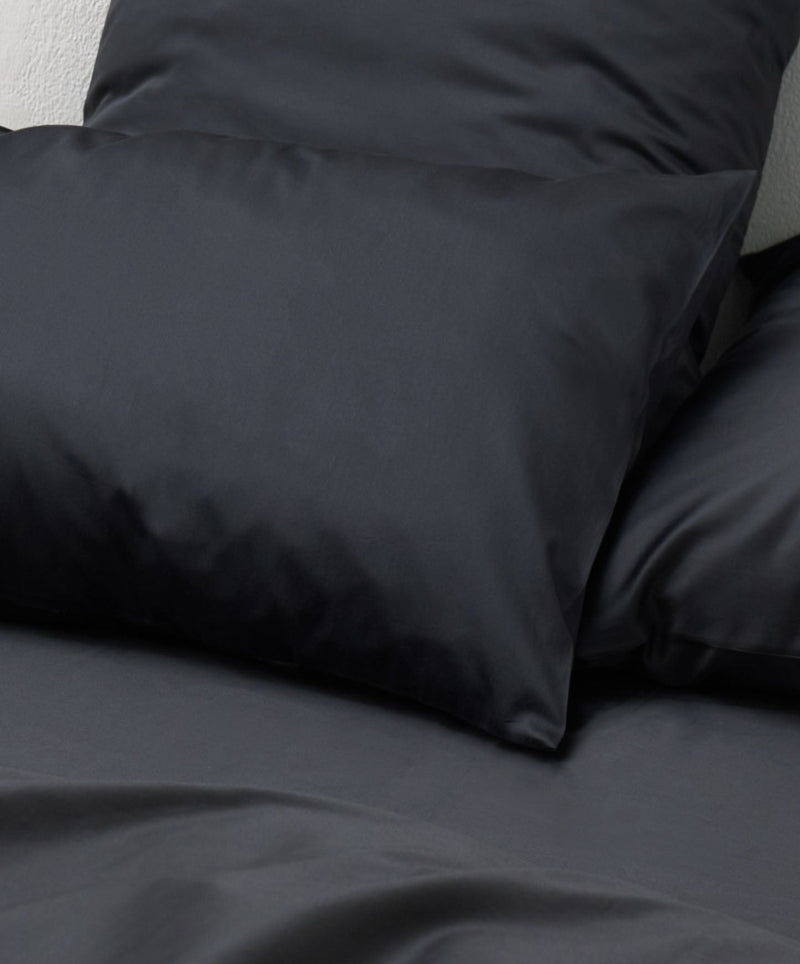 Close-up of the Cotton Sateen Bed Set in Graphite by MOST on a bed, showcasing its sleek, luxurious appearance. The glossy finish enhances its elegance, making it perfect for contemporary or minimalist designs.