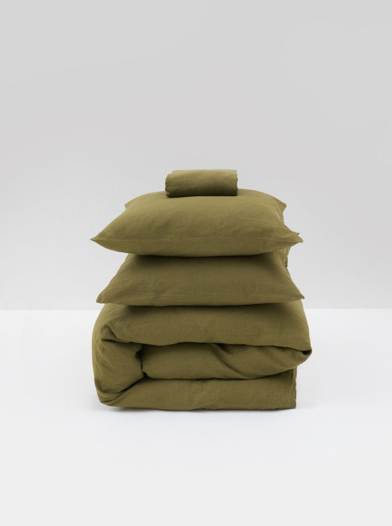 A neatly folded set of MOST Washed Linen Bed Set in Olive, including a comforter cover and pillowcases, stacked against a clean, white background.