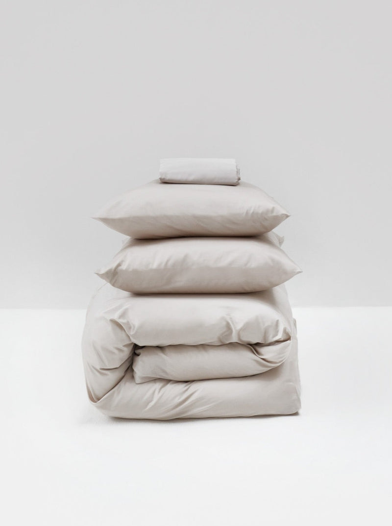 A stack of neatly folded MOST Cotton Sateen Bed Set in Sand bedding items including sheets, pillowcases, and a comforter cover against a plain white background.