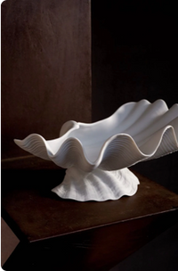 Elegant white ceramic bowl in the shape of a seashell, displayed on a wooden surface.