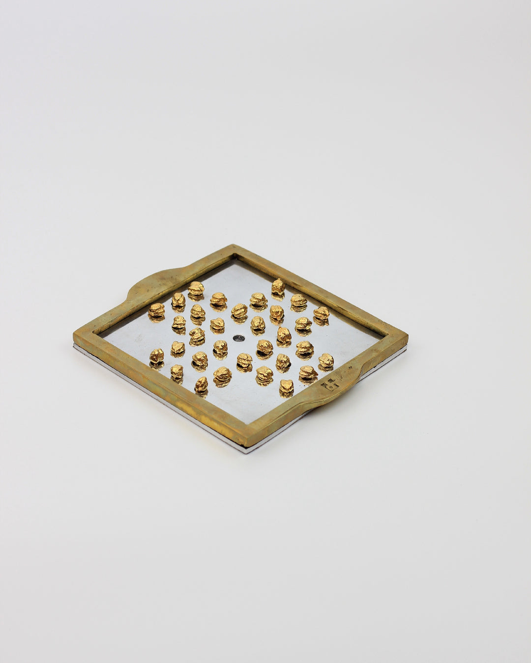 Solitario Inglés — side angle of brass game board with pegs