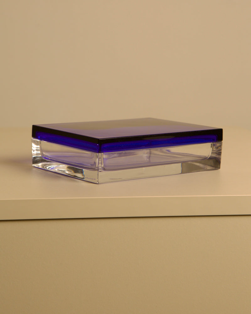 The Treaptyque Italian Box in transparent and blue crystal by Duccio Di Segna from the 80’s sits on a smooth, light surface with a plain beige background, showcasing its rectangular shape and striking deep blue lid.