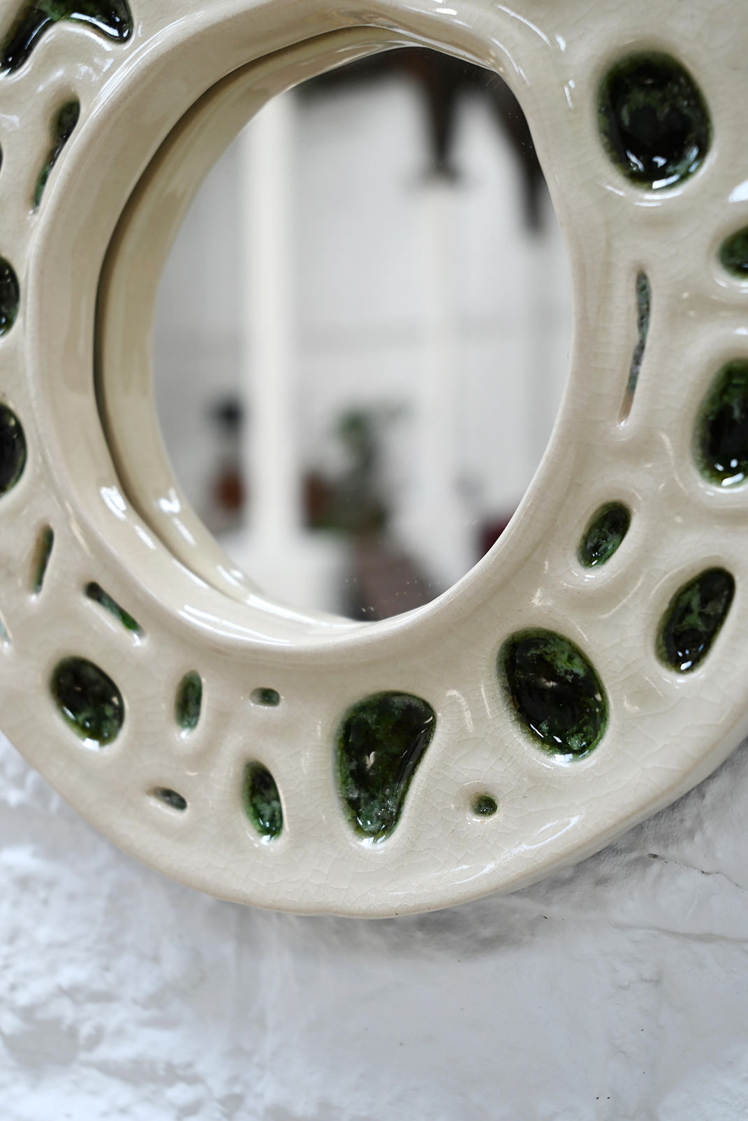 Close-up detail of cream ceramic mirror frame with green glazed holes