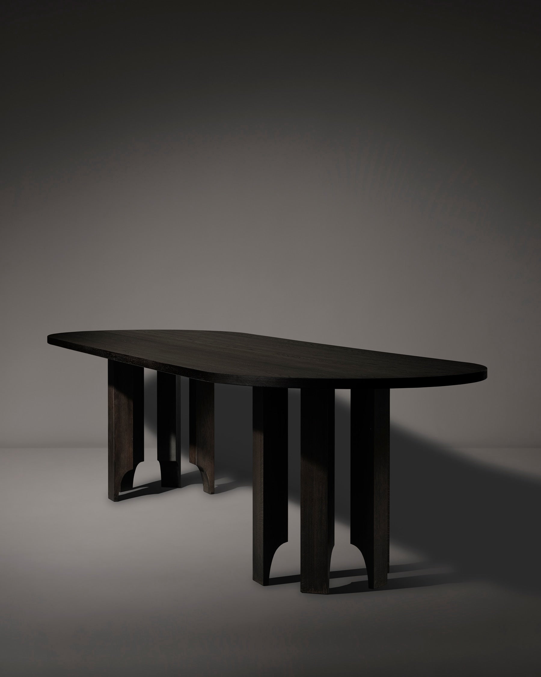 The Mokko Acer Capsule Table features a smooth, elongated oval top crafted from solid European oak with four uniquely shaped sturdy legs, shown against a softly lit gray background.