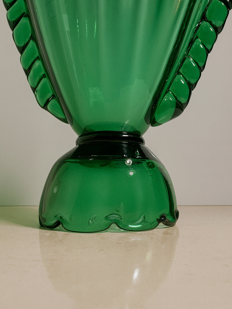 A close-up of the base and lower part of the Dodo Vintage Glass Amphora Vase -1910s, featuring handmade green glass with decorative scalloped edges, displayed on a light-colored surface against a neutral background.