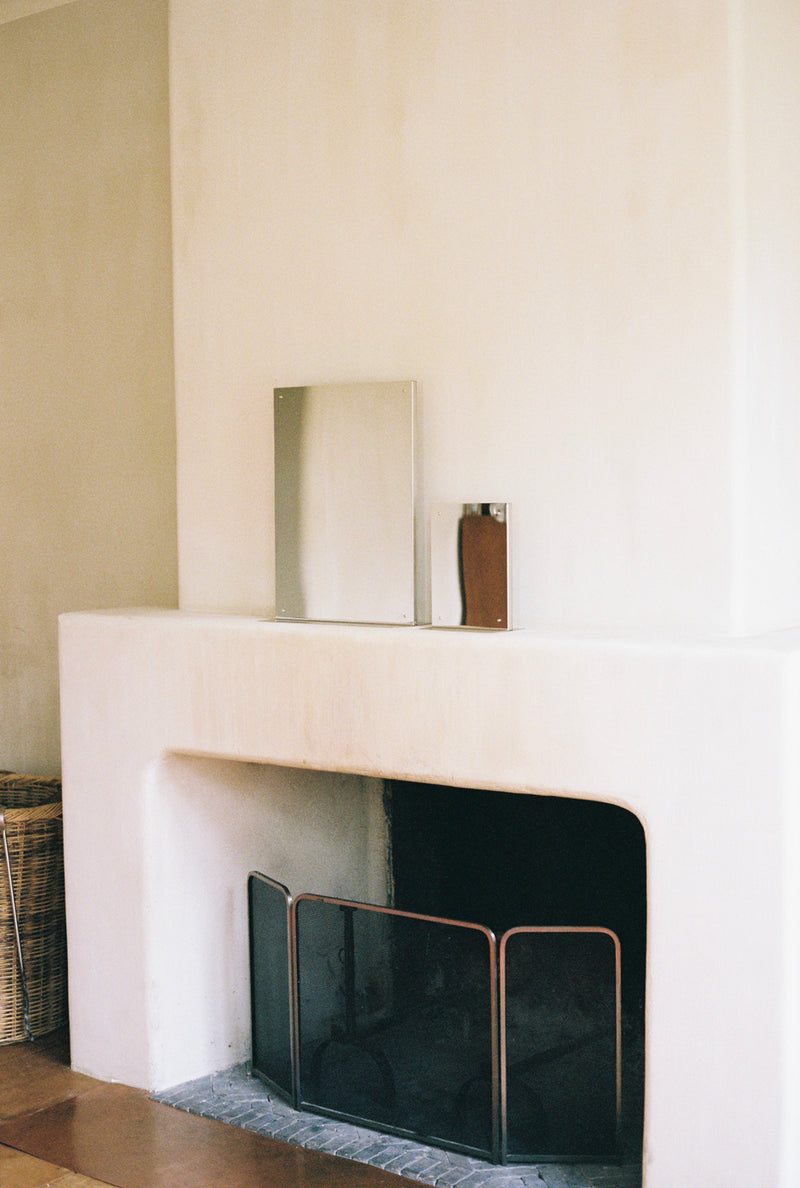 Medium flat mirror displayed on white fireplace mantel with amber bottle
